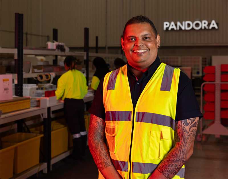 Praneel Sharma, Pandora's Head of Supply Chain ANZ, stands in Pandora's warehouse, smiling.